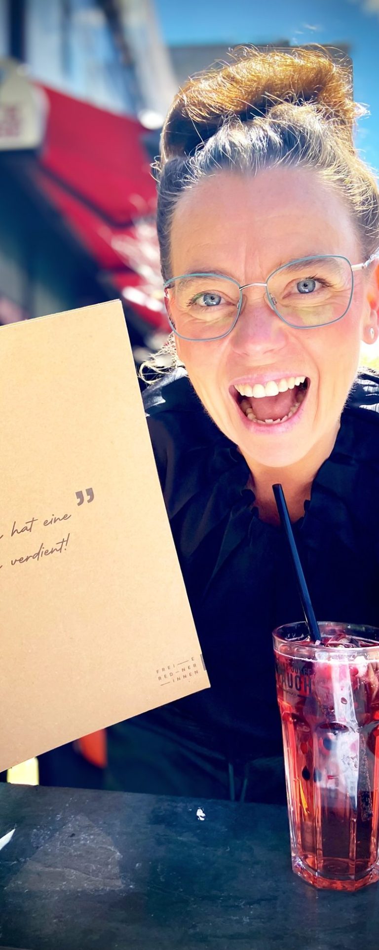 Kati Kreyser, lächelnd und strahlend nach bestandener IHK Prüfung zur Freien Rednerin  und ein Glas Limonade.